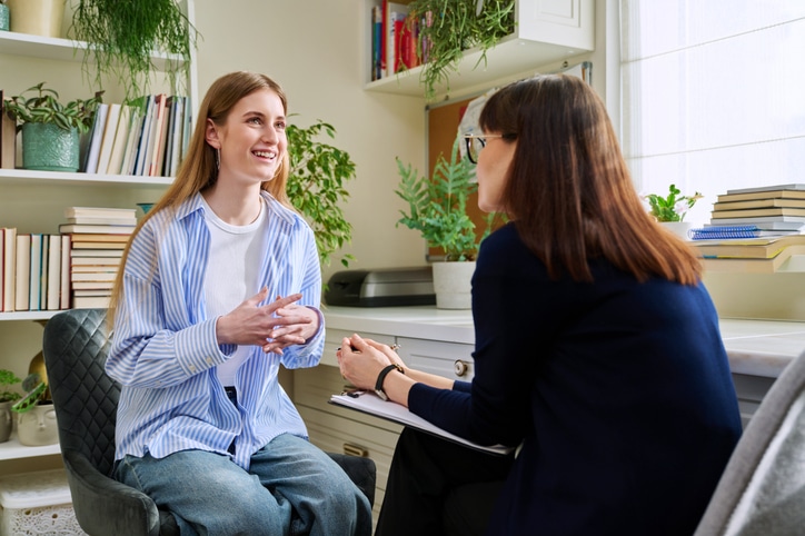 Smiling young teenage female patient talking to professional mental therapist Smiling positive young teen female patient talking to professional mental therapist. Teenager girl high school college student in therapy with psychologist psychotherapist counselor. Treatment support