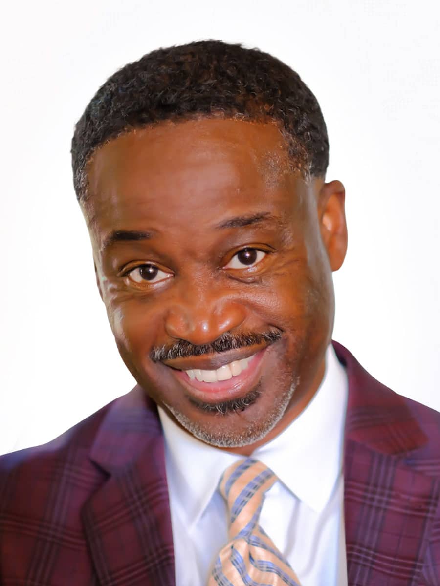 A smiling man with short curly hair, wearing a maroon plaid suit jacket, white shirt, and light-colored striped tie, poses confidently against a plain white background—perfect for Kenneth Gardner, LLP's professional image.