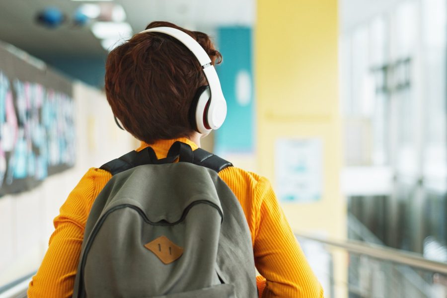 Child wearing headphones and a backpack walking down a school hallway, representing Asperger's Syndrome testing and therapy in Ann Arbor