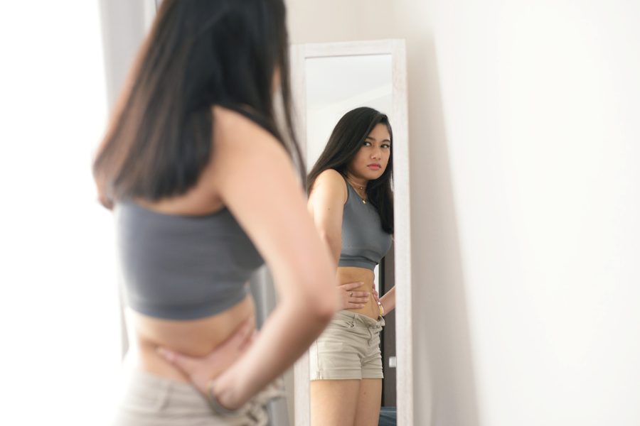 Woman studying her reflection in a full-length mirror, illustrating body image concerns addressed through therapy at Ann Arbor Therapy & Testing