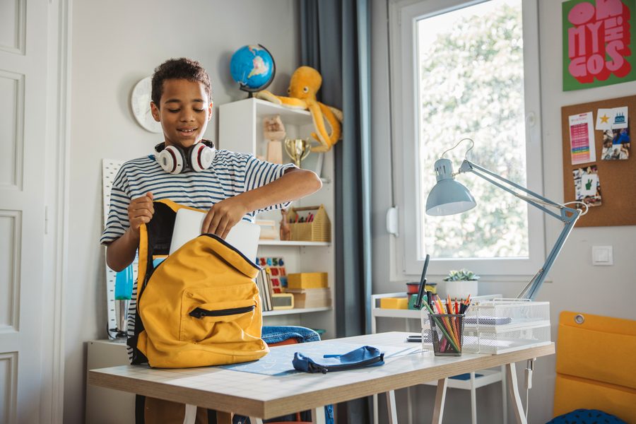 Smiling boy packing his backpack at a desk at home, getting ready for school with support from developmental and school readiness testing